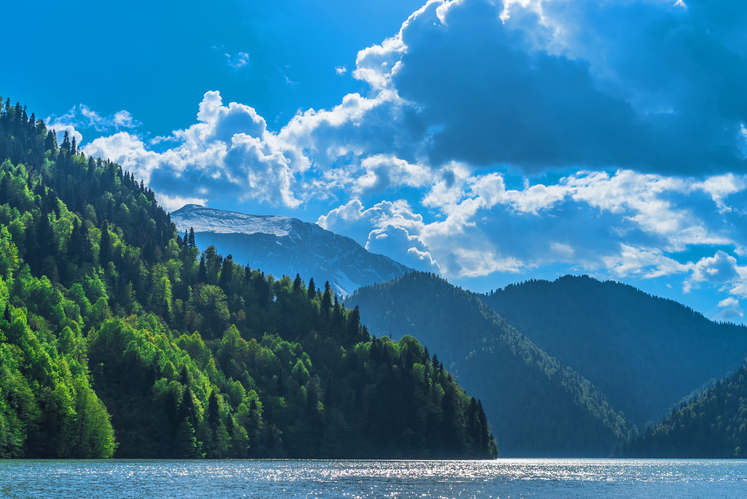 Beautiful Lake Ritsa in the Caucasus Mountains. Green mountain hills, blue sky with clouds. Spring landscape